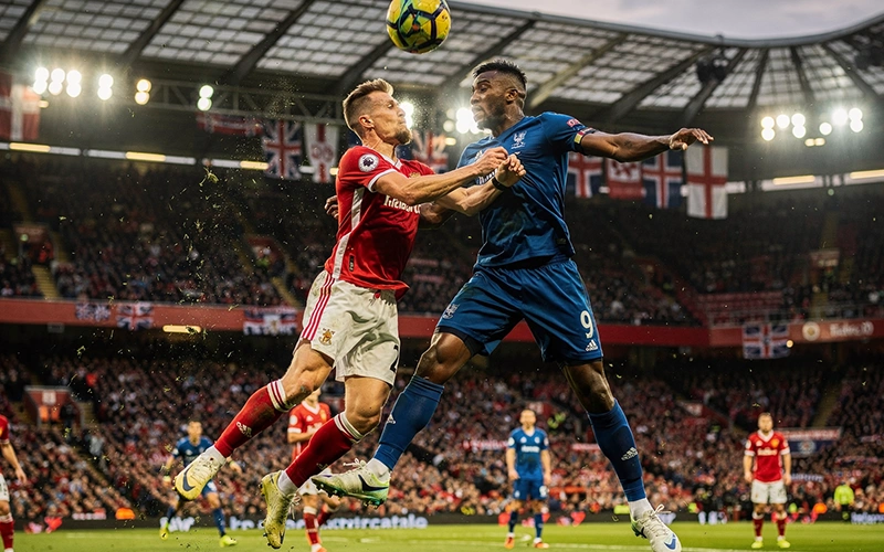 Avant-centre puissant disputant un duel aérien dans un stade anglais